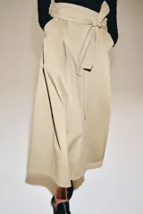 Falda midi color beige confeccionada en hilatura con mezcla de algodón. Presenta tiro medio, cintura con trabillas, bolsillos laterales ocultos en costura y cinturón del mismo tejido. Su diseño incluye un bajo acabado en línea evasé y cierre lateral con cremallera.