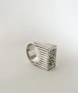 Anillo tipo sello de plata 950 con diseño de líneas horizontales y cristales verdes incrustados.