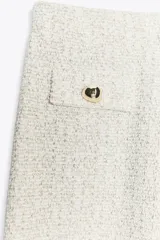 Pantalón de tiro medio, pierna ancha, confeccionado en tejido texturado de color claro con hilo metalizado. Presenta falsos bolsillos delanteros con botones metálicos dorados.