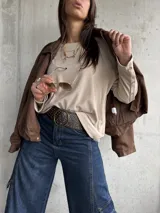 Remera de lanilla color beige, de corte holgado y manga larga. Presenta una hilera de botones decorativos a lo largo de toda la parte externa de las mangas.