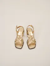 Sandalias de cuero color dorado, con taco bajo, puntera cuadrada y tiras cruzadas en el empeine con textura de pespuntes. Cuentan con tira ajustable en el talón con hebilla metálica.