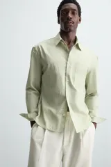 Camisa de hombre de corte relajado (relaxed fit) en color verde menta pálido, confeccionada en tejido con textura irregular acanalada. Presenta cuello solapa, manga larga con puño abotonado, bolsillo plastrón en el pecho y bajo asimétrico con aberturas laterales.