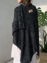 Ruana tejida en punto jersey, confeccionada en hilo de algodón con destellos de lurex, presenta un diseño envolvente y etiqueta de marca en cuero sintético.