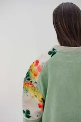 Campera larga con cierre metálico y bolsillos grandes, de color verde con mangas y parte inferior estampadas con diseño abstracto multicolor.