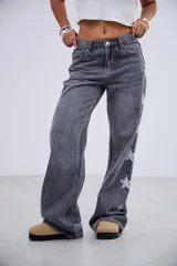 Jean de corte recto y tiro medio-bajo, color gris lavado, con detalle de estrellas bordadas a lo largo de los laterales externos de las piernas.