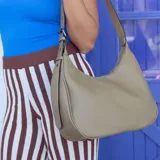 Cartera tipo hobo o media luna de cuero sintético negro, con textura granulada. Posee una correa ajustable para llevar al hombro o cruzada.