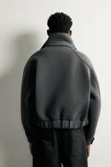 Cazadora boxy fit de tejido técnico gris oscuro, con cuello subido envolvente, cierre frontal asimétrico con cremallera oculta y bolsillos de vivo en la cadera.