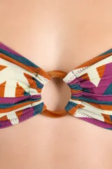 Top de bikini bandeau con estampado geométrico multicolor en tonos terracota, violeta, verde azulado y blanco. Cuenta con tirantes para anudar al cuello y una argolla circular de carey en el centro del busto.