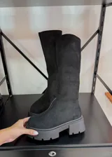 Botas bucaneras de color negro con caña alta confeccionada en tela elástica tipo gamuza y suela track de goma gruesa.