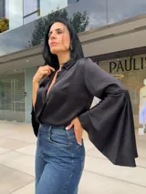 Blusa negra de manga larga con cuello camisero y puños acampanados o con aberturas.