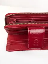 Billetera grande de cuero vacuno con textura granulada y detalles en charol. Cuenta con múltiples ranuras para tarjetas y cierre de solapa con broche a presión grabado con el logo de la marca.