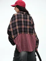 Camisa de corte relajado con diseño combinado. La parte superior presenta un estampado a cuadros en tonos marrones y negros, mientras que la parte inferior destaca por un panel de rayas verticales en color bordó. Cuenta con cierre frontal de botones y mangas largas.