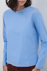 Remera de manga larga color marrón, con costuras a la vista en color blanco que resaltan los cortes de la prenda. Presenta un pequeño bordado blanco en la parte inferior y un corte recto.