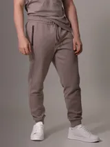 Pantalón de jogging color topo, con cintura elástica ajustable con cordón, puños ajustados y bolsillos laterales con cierre.