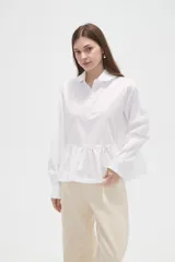 Camisa de manga larga con estampado de rayas verticales en azul marino y rojo. Presenta cuello camisero, cierre frontal con botones y un diseño con volado en la cintura que aporta volumen.
