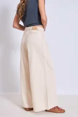 Pantalón de jean color crudo, de corte palazzo y tiro alto, con bolsillos laterales y traseros. Se ajusta a la cintura con cinturón de cuero marrón con hebilla dorada.