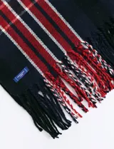 Bufanda de estilo escocés con diseño de cuadros en tonos verde, azul y líneas finas en rojo. Presenta flecos en los extremos y una etiqueta pequeña de la marca.