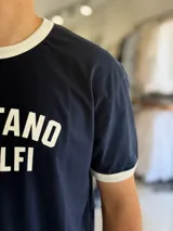 Remera de algodón pesado de corte oversize en color blanco, con cuello redondo y ribetes en las mangas de color azul marino. Cuenta con un estampado frontal con el texto "POSITANO AMALFI".