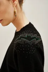 Sweater negro de punto con cuello redondo, manga larga y detalle de tachas metálicas en los hombros formando un diseño de rayo.