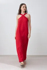 Vestido largo rojo, sin mangas, con escote halter cruzado en el frente y caída recta y holgada.