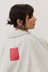 Chaqueta oversize de gabardina color verde claro, con solapa clásica, bolsillos frontales, cierre de botones oscuros y mangas largas con vuelta en tono verde lima vibrante.