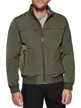 Campera bomber verde militar de poliéster, con cuello mao, cierre frontal con cremallera, dos bolsillos laterales con cremallera, puños y ruedo elásticos. Logo de Tommy Hilfiger bordado en el pecho.