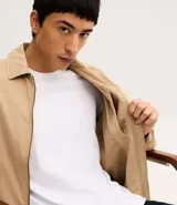 Campera tipo bomber de sarga color beige, con cuello inglés, cierre frontal de cremallera y puños y cintura ajustados con elástico en tono contrastante.