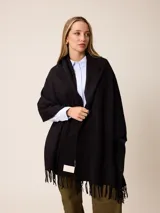 Pashmina de textura suave y color crema, con diseño liso y terminaciones en flecos en los extremos. Incluye una etiqueta decorativa en una de las esquinas.