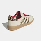 Championes Adidas modelo Handball Spezial, con diseño clásico de perfil bajo. Presentan una base en tono beige con detalles de estampado animal print en las icónicas tres tiras laterales y en el talón. Incluyen cordones en color rojo vibrante, forro interior a tono y suela de caucho tipo goma.