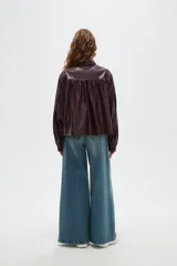 Chaqueta de eco-cuero color marrón oscuro, con cuello camisero, cierre frontal con botones, mangas largas abullonadas con puños y detalles de frunces en los hombros.