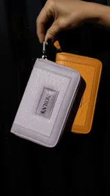 Billetera mediana de cuero sintético con textura tipo croco y cierre perimetral. Cuenta con compartimentos internos para tarjetas y monedero con cierre. Incluye una etiqueta frontal con el logo de la marca.