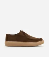 Championes de estilo casual con diseño moc toe, confeccionadas en cuero gamuza color marrón. Presentan costura visible en la puntera, cierre con cordones y suela de goma en tono beige de perfil bajo.