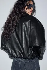 Chaqueta estilo bomber de efecto piel en color verde oliva, con cuello solapa, cierre frontal con cremallera, mangas largas y bajo elástico.