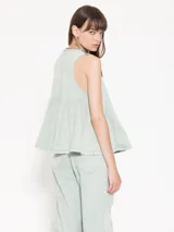 Top sin mangas color celeste claro, confeccionado en gabardina, con escote delantero ajustable mediante cordón y ojalillos. Presenta recortes triangulares que generan vuelo en la parte inferior.