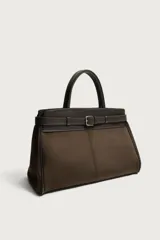 Bolso de mano estructurado en color marrón, confeccionado en una combinación de materiales que incluye gamuza en el cuerpo principal y cuero en la parte superior y asas. Presenta un detalle de cinturón decorativo con hebilla metálica plateada en la parte frontal, doble asa de mano y cierre principal con imán.
