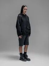 Hoodie oversize color negro, confeccionado en frisa gamuzada de algodón con recortes en hombros y bolsillo frontal tipo cargo con solapa en material técnico. Presenta capucha forrada y puños y ruedo acanalados.