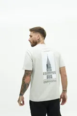 Remera de manga corta color beige con estampado gráfico en la espalda que representa el edificio Chrysler de Nueva York y texto descriptivo.