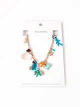 Collar de cadena dorada con múltiples dijes colgantes de temática marina, incluyendo caracoles, corales de colores, una tortuga y borlas decorativas.