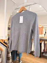 Media polera de tejido fino color gris, con cuello alto, manga larga y corte ajustado al cuerpo.