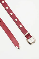 Cinturón de cuero vacuno color bordó, con diseño de apliques metálicos en forma de corazón y hebilla plateada con logo de la marca grabado.