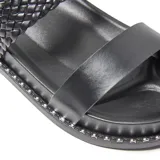 Sandalias de plataforma baja color negro, con dos tiras anchas en el empeine: una frontal lisa y otra trasera de diseño trenzado. La suela cuenta con un detalle de pequeñas tachas metálicas plateadas en todo el contorno.