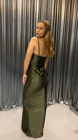 Vestido largo verde oliva de satén, con breteles finos, escote recto y abertura en la pierna. Presenta un corte en la zona del abdomen.