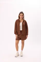 Conjunto deportivo compuesto por un buzo con cierre frontal, capucha y bolsillos, y un short con cintura elástica y cordón ajustable. Confeccionado en tejido soft premium de color marrón.