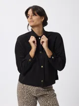 Campera de estilo camisero con textura efecto gamuzado, color negro. Presenta cuello clásico, cierre frontal con botones metálicos, bolsillos aplicados en el pecho y mangas largas con puños abotonados.
