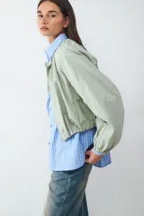 Campera de nylon manga larga en color verde militar, con cuello redondo, cierre frontal de cremallera y diseño fruncido con bajo elástico.