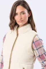 Chaleco de sherpa color crema con cierre frontal y detalles de terminación en cuero sintético color beige. Diseño sin mangas con cuello alto.