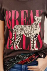 Remera de algodón marrón oscuro con estampa frontal que presenta un leopardo y la inscripción en tono fucsia.