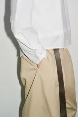 Camiseta oversize de cuello redondo y manga larga con puños abotonados. Confeccionada en algodón, presenta un diseño con combinación de tejidos a tono y bajo asimétrico.