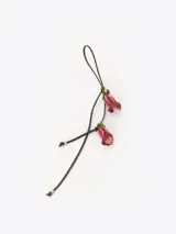 Charm decorativo compuesto por un cordón fino de cuero oscuro con dos dijes colgantes en forma de flores, elaborados artesanalmente con cuentas de cristal rosadas y detalles en hilo verde.