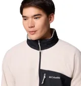 Campera de polar Columbia con cierre frontal completo, cuello alto y bolsillo en el pecho con cierre. Presenta un diseño en color beige con detalles en negro en el bolsillo, cuello, puños y dobladillo.